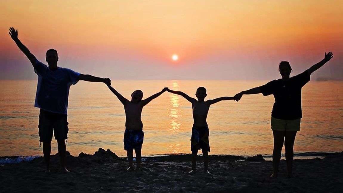 Familie hält sich bei Sonnenuntergang am Strand an den Händen.